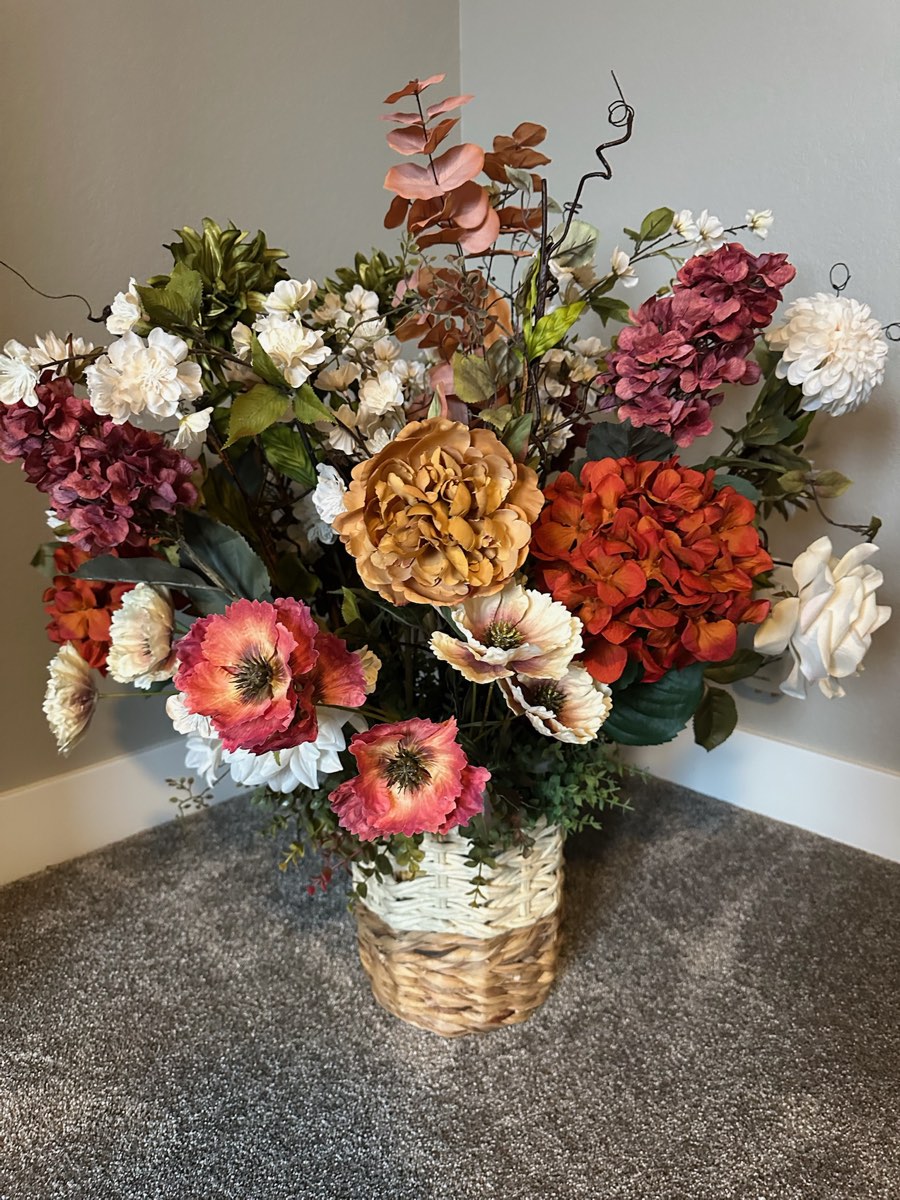 Large faux arrangement of burgundy, rust and cream blooms in a tall woven basket